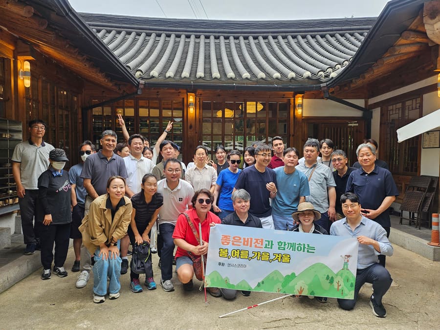 한옥 앞 단체사진, "좋은비전과 함께하는 봄,여름,가을,겨울 후원 앤시스코리아" 현수막을 흰지팡이를 든 참가자가 들고 있음