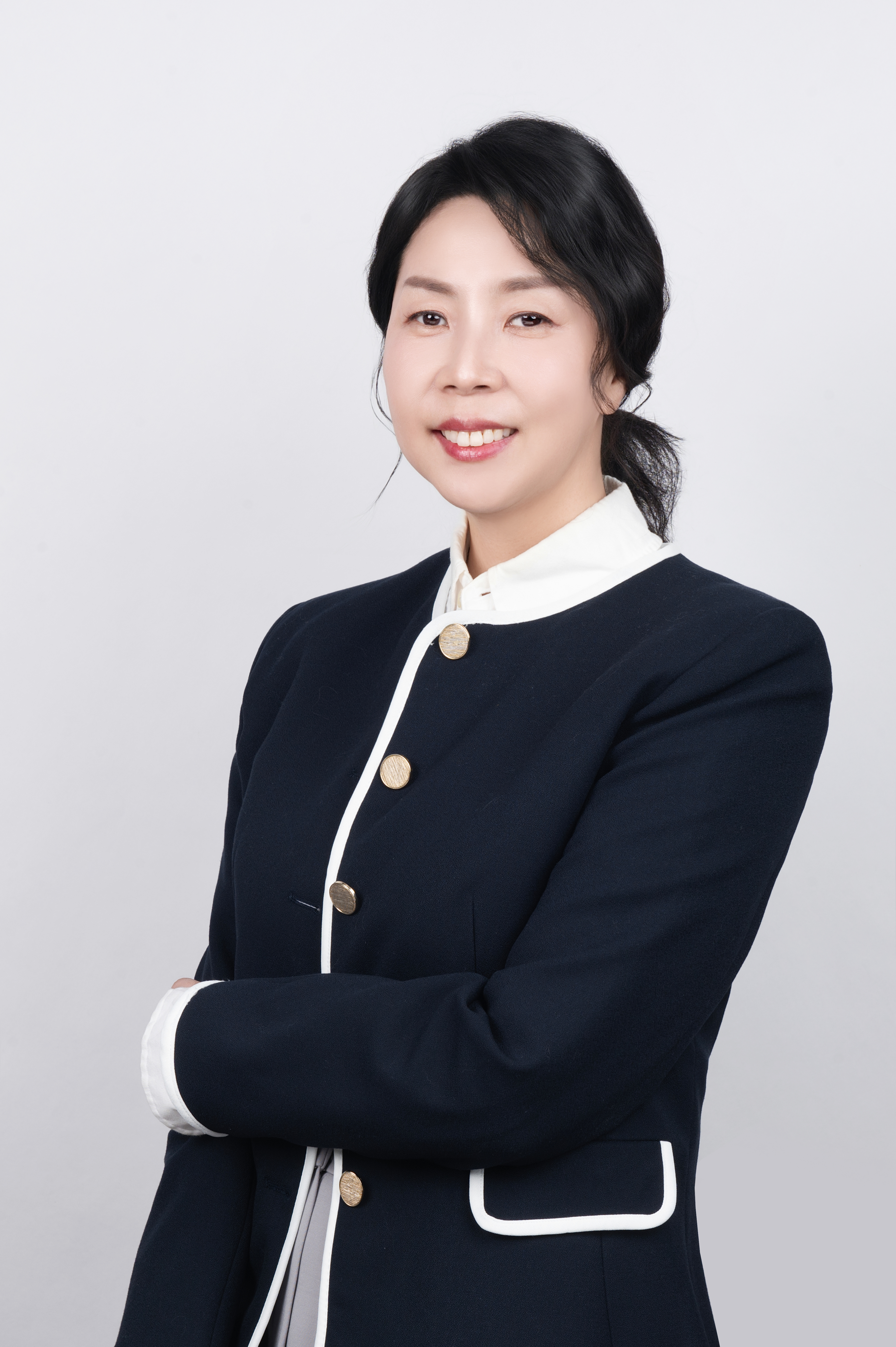 김기현 강사 사진-흰색 장식이 있는 짙은색 재킷을 입고 있다. 머리를 뒤로 묶고 팔짱을 낀 채 정면을 바라보며 밝게 미소 짓고 있다.